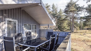 A covered outdoor patio with a table and chairs, a wooden deck, and a view of trees and open land.