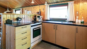 A compact kitchen with wooden cabinets, a stove, a sink, and a window with curtains.