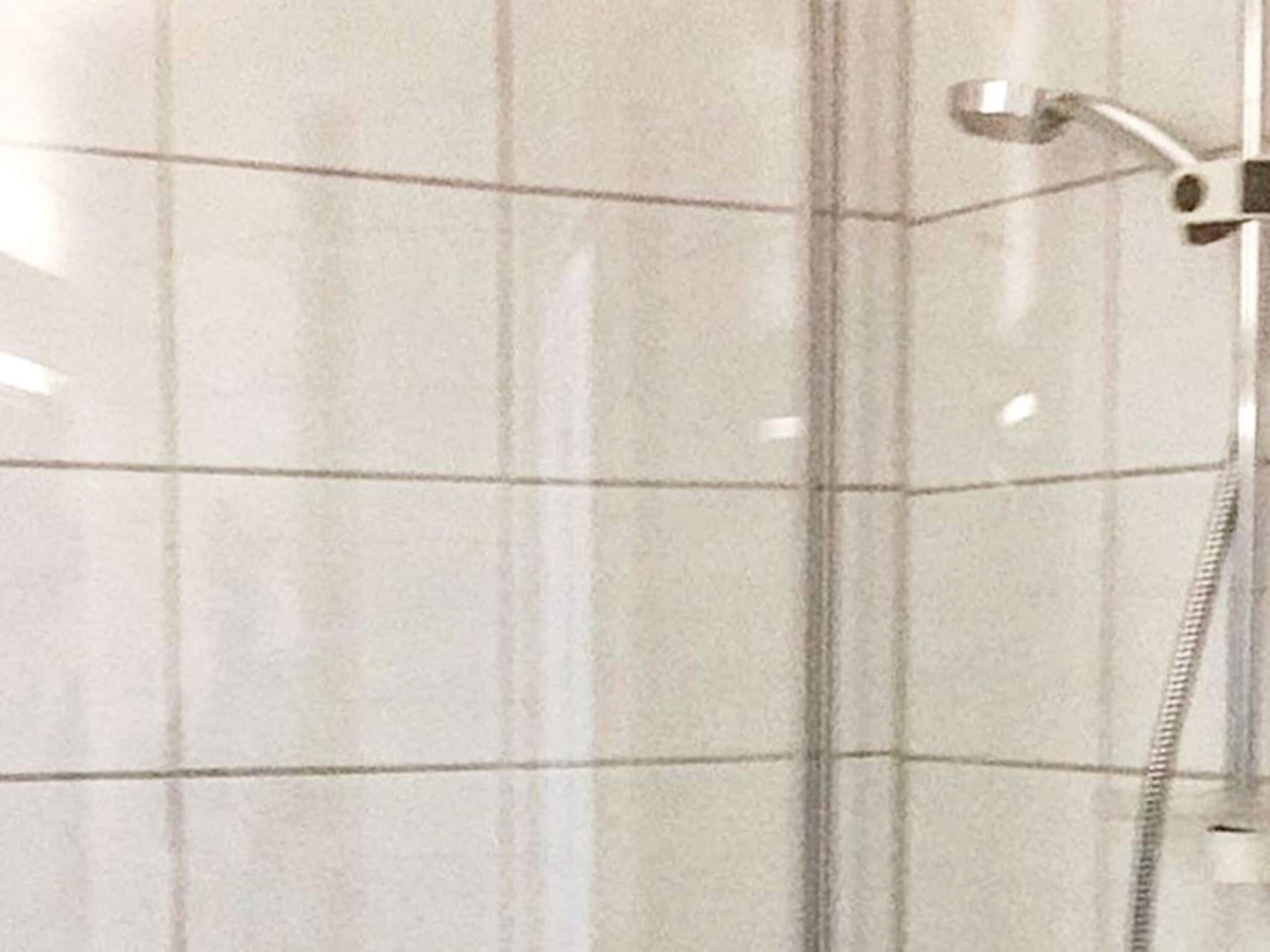 Une salle de bain avec des murs carrelés de carreaux blancs et une douche équipée d’un pommeau de douche à main.