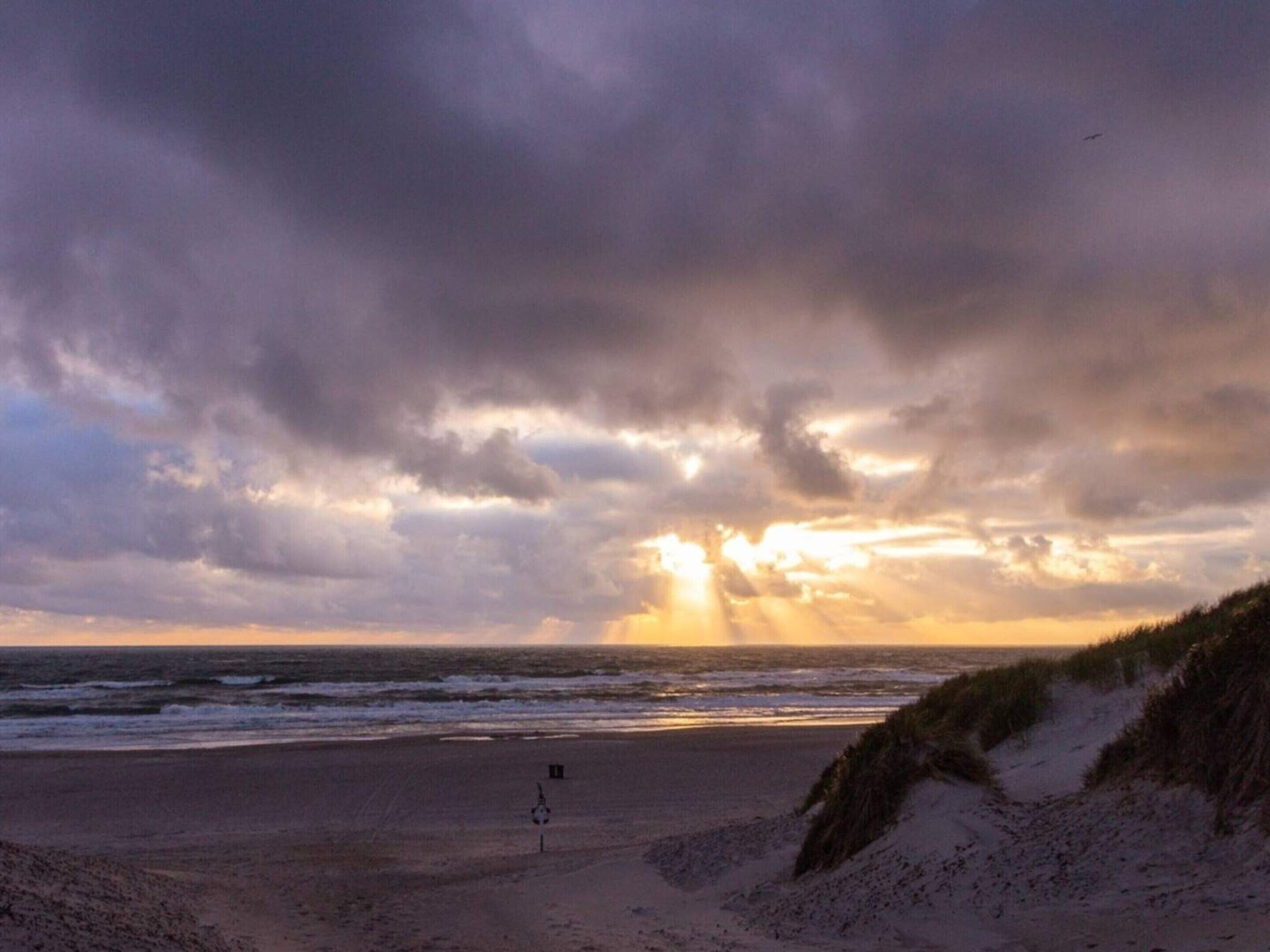 En strand med ett badvakts torn, sanddyner och havet under en molnig himmel.