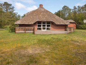 A thatched-roof building with a brick exterior, a wooden deck, and a glass door entrance. - Holiday Home in NÃ¸rre Nebel (Norre Nebel)