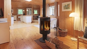 A wooden cabin interior with a central wood-burning stove, a kitchen area, and a dining space. - 6 Person Holiday Home in Gilleleje (Gilleleje)