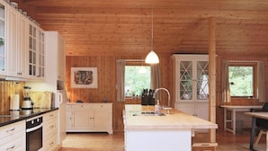 A wooden cabin interior with a kitchen, dining area, and a large window. - 6 Person Holiday Home in Gilleleje (Gilleleje)