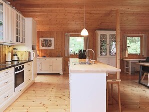 A wooden cabin interior with a kitchen, dining area, and a large window.