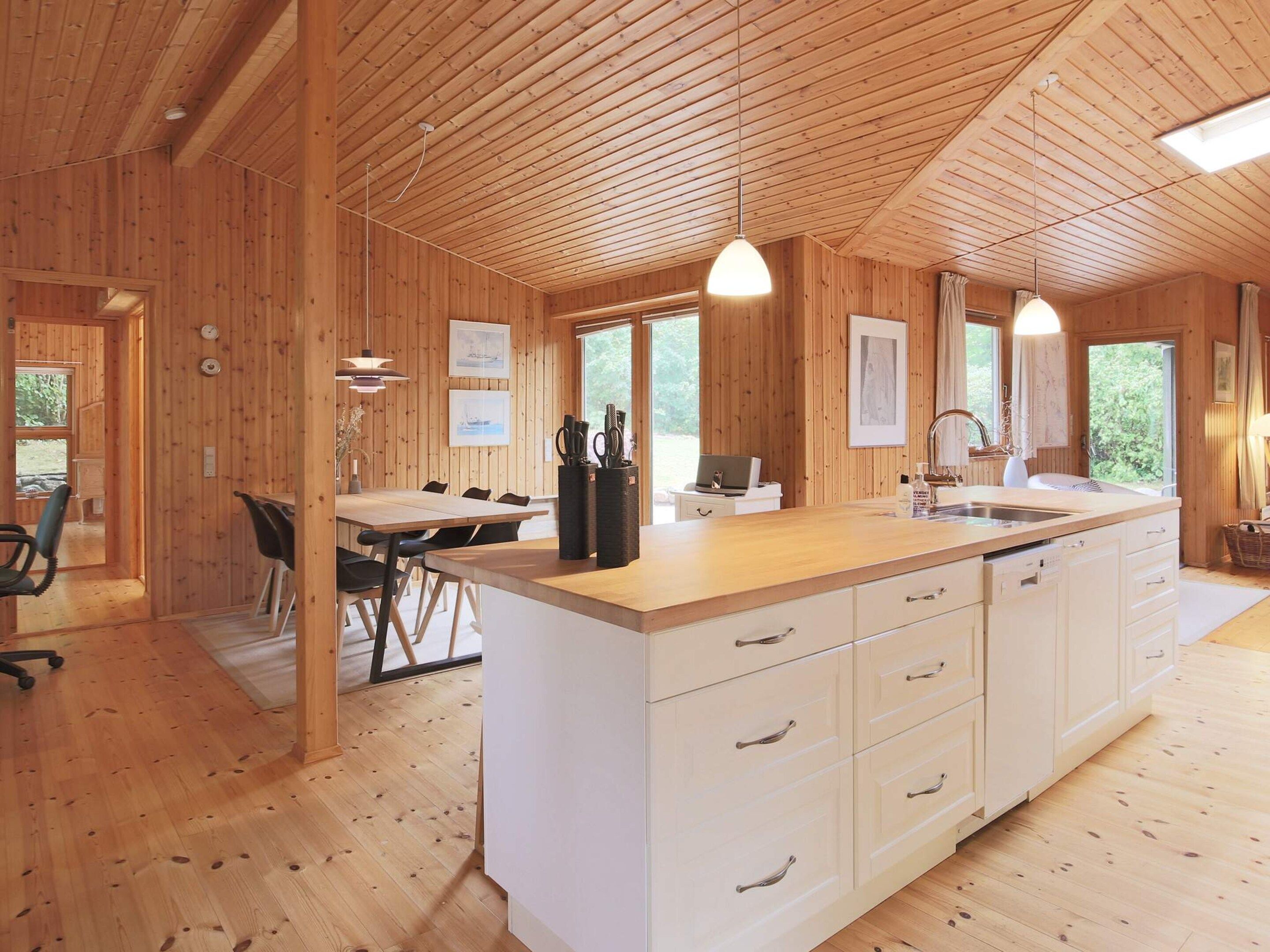A wooden interior with a kitchen island, dining area, and a large window.