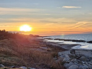 A coastal landscape with a sunset, rocky shoreline, and sparse vegetation. - 6 Person Holiday Home in Gilleleje (Gilleleje)