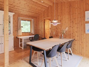 A wooden-paneled room with a large table and chairs, a window with curtains, and a hanging light fixture. - 6 Person Holiday Home in Gilleleje (Gilleleje)
