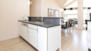 A modern kitchen with a central island, white cabinetry, and a dining area with a table and chairs. - Holiday Home in GroÃŸenbrode (Grossenbrode)