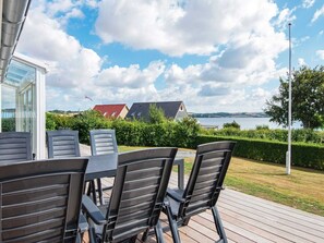 Een terras met een tafel en stoelen, met uitzicht op een meer en huizen op de achtergrond.