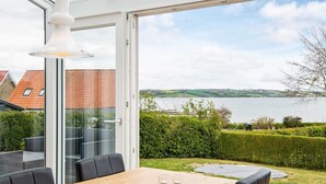 Een eethoek met een tafel en stoelen, een glazen deur die uitkomt op een uitzicht over een meer en gebouwen.
