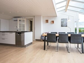 A modern kitchen with a central island, a dining area with a wooden table and chairs, and a skylight above. - 6 Person Holiday Home in Broager (Broager)