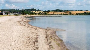 Een zandstrand met een kalm meer, een rij huizen op de achtergrond en een gedeeltelijk bewolkte lucht.