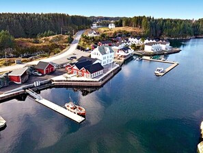 Un village côtier doté d’un quai, d’un bateau et de plusieurs bâtiments, dont une grande maison blanche.