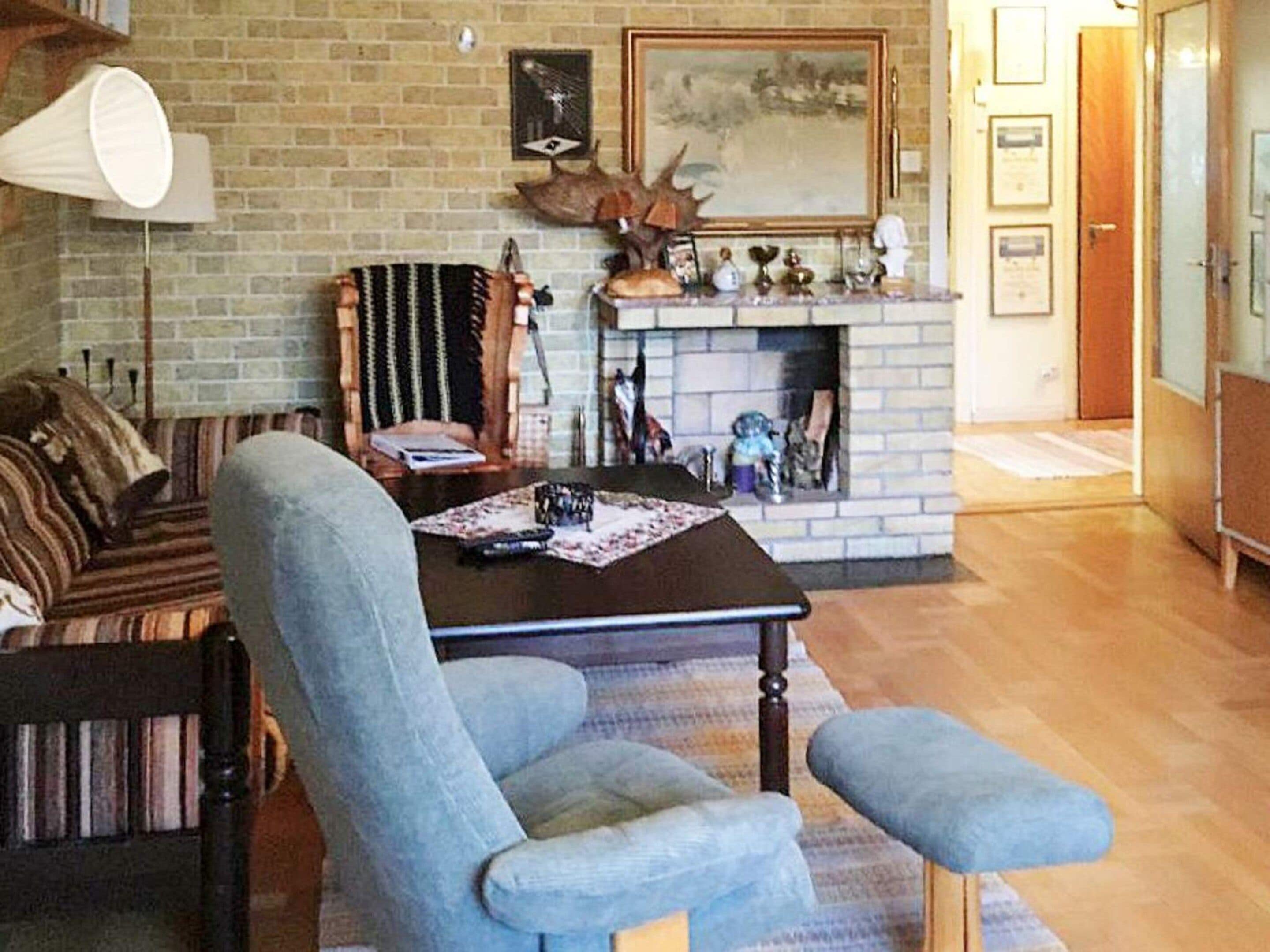 A living room with a brick fireplace, a sofa, a table with a lamp, and a chair.