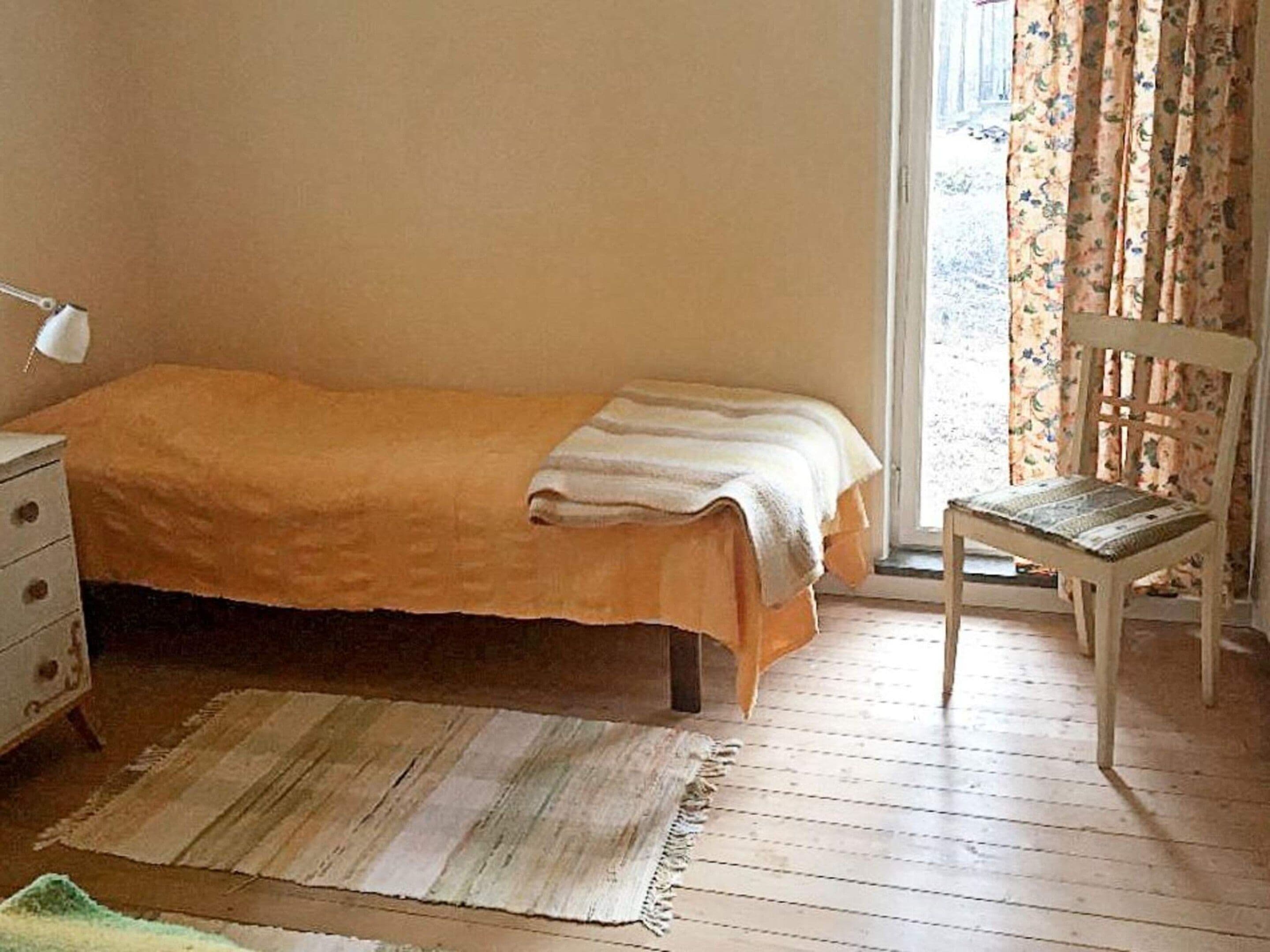 A bedroom with a bed, a chair, a dresser, and a window with curtains.