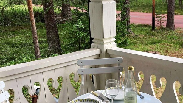 A white wooden deck with heart-shaped cutouts, a round table with a bottle of white wine, a glass, and a plate. - 6 Person Holiday Home in Rorbacksnas (Lima)