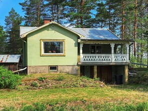 Uma casa de dois andares com fachada verde, varanda com grades decorativas e telhado de metal.