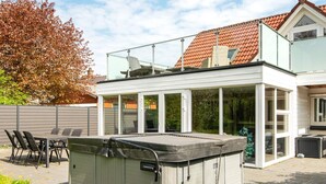 A modern house with a glass conservatory, a hot tub, and a patio with outdoor furniture. - 8 Person Holiday Home in Henne (Henne)
