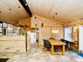 Una cocina moderna con pared de ladrillo, techo de madera y zona de comedor con mesa y sillas de madera.