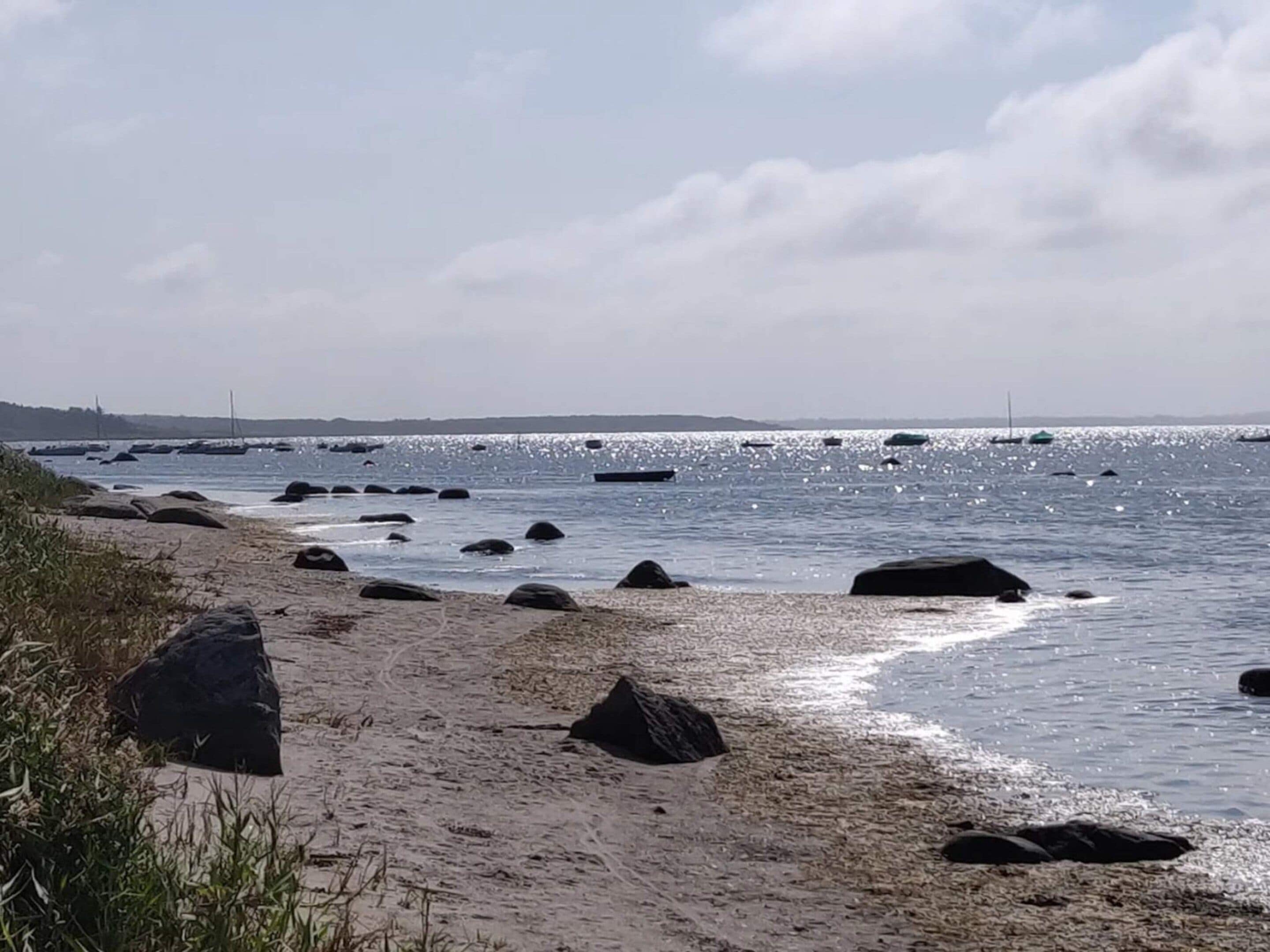 A beach with rocks and boats in the water.