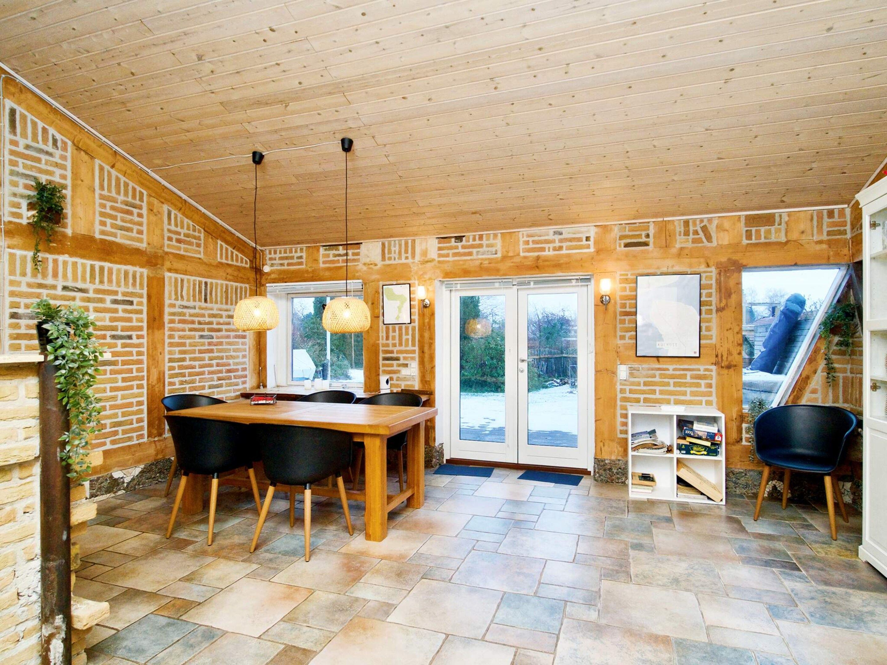 A dining area with a wooden table and chairs, a brick wall, and a view through a glass door.