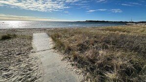 En kyststi der fører til en strand med klar himmel og fjerne kystlinjer.