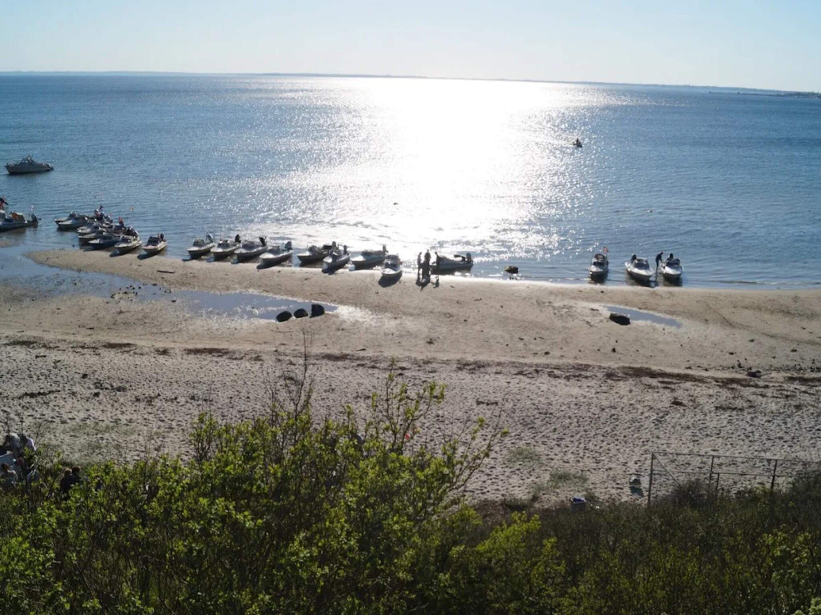 A beach with boats and people, clear sky, and calm sea.