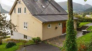 Ett tvåvåningshus med ett sluttande tak, en skorsten och en liten veranda med ett bord och en stol.