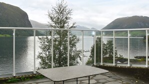 En uteplats med ett stengolv, ett metallbord och stolar, med utsikt  över en sjö och berg i bakgrunden.