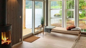 A cozy room with a fireplace, large windows overlooking a lake, and a bench with cushions. - 8 Person Holiday Home in Skei i Jolster (Sunnfjord)