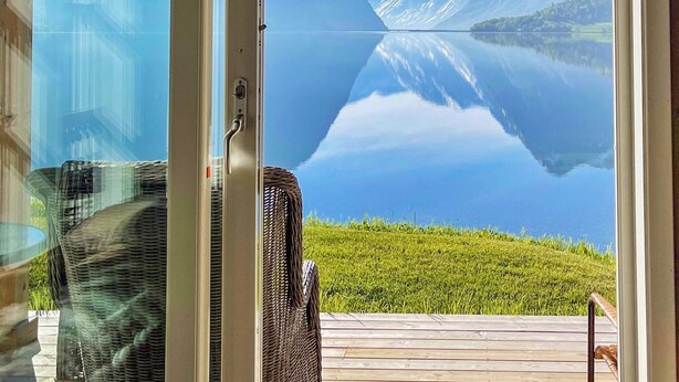 A room with a large glass door leading to a view of a mountain lake. - 8 Person Holiday Home in Skei i Jolster (Sunnfjord)
