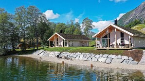 A lakeside cabin with a deck, a covered porch, and a stone retaining wall. - 8 Person Holiday Home in Skei i Jolster (Sunnfjord)