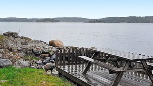 A wooden deck with picnic tables overlooking a calm lake, surrounded by rocks and sparse vegetation.
