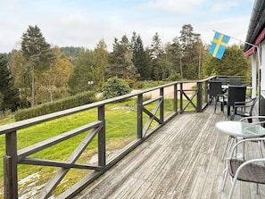 A wooden deck with outdoor furniture, a flag, and a view of a forested area. - 6 Person Holiday Home in Henan (Henån)
