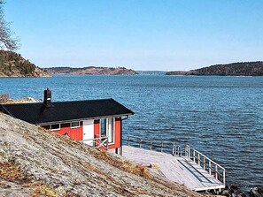 A red building with a black roof, a wooden dock, and a calm body of water. - 6 Person Holiday Home in Henan (Henån)