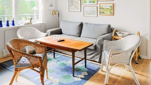 A cozy living room with a grey sofa, wicker chairs, a wooden coffee table, and a blue patterned rug.