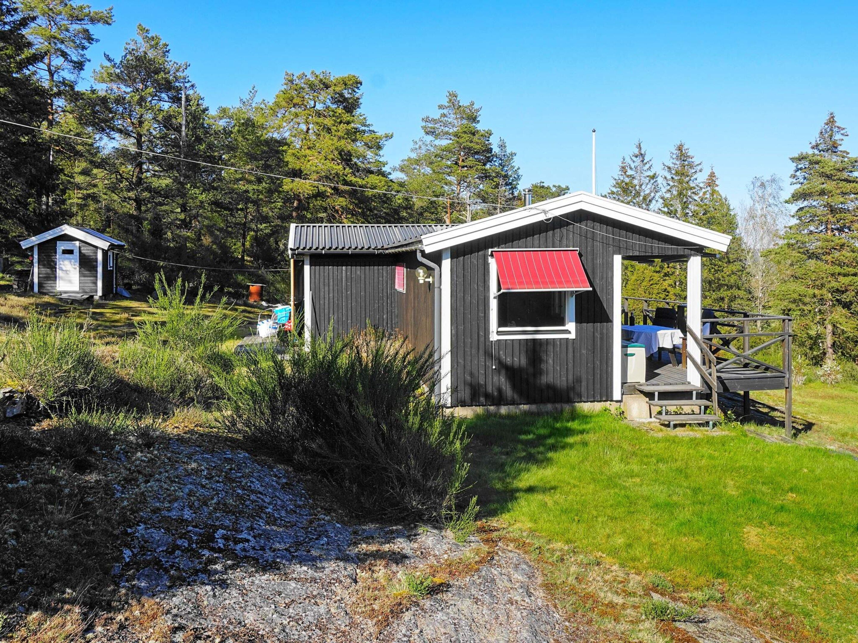 A small wooden cabin with a red awning, a deck, and a gravel path leading to it.