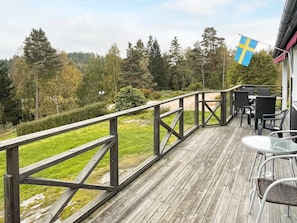 A wooden deck with outdoor furniture, a flag, and a view of a forested area. - 6 Person Holiday Home in Henan (Henån)