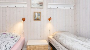 A bedroom with two beds, a wicker ottoman, wall-mounted sconces, and framed artwork. - 5 Person Holiday Home in Hejls (Hejls)