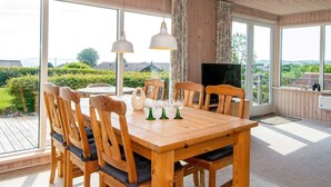 A wooden dining table with chairs, a TV, and large windows overlooking a garden. - 5 Person Holiday Home in Hejls (Hejls)