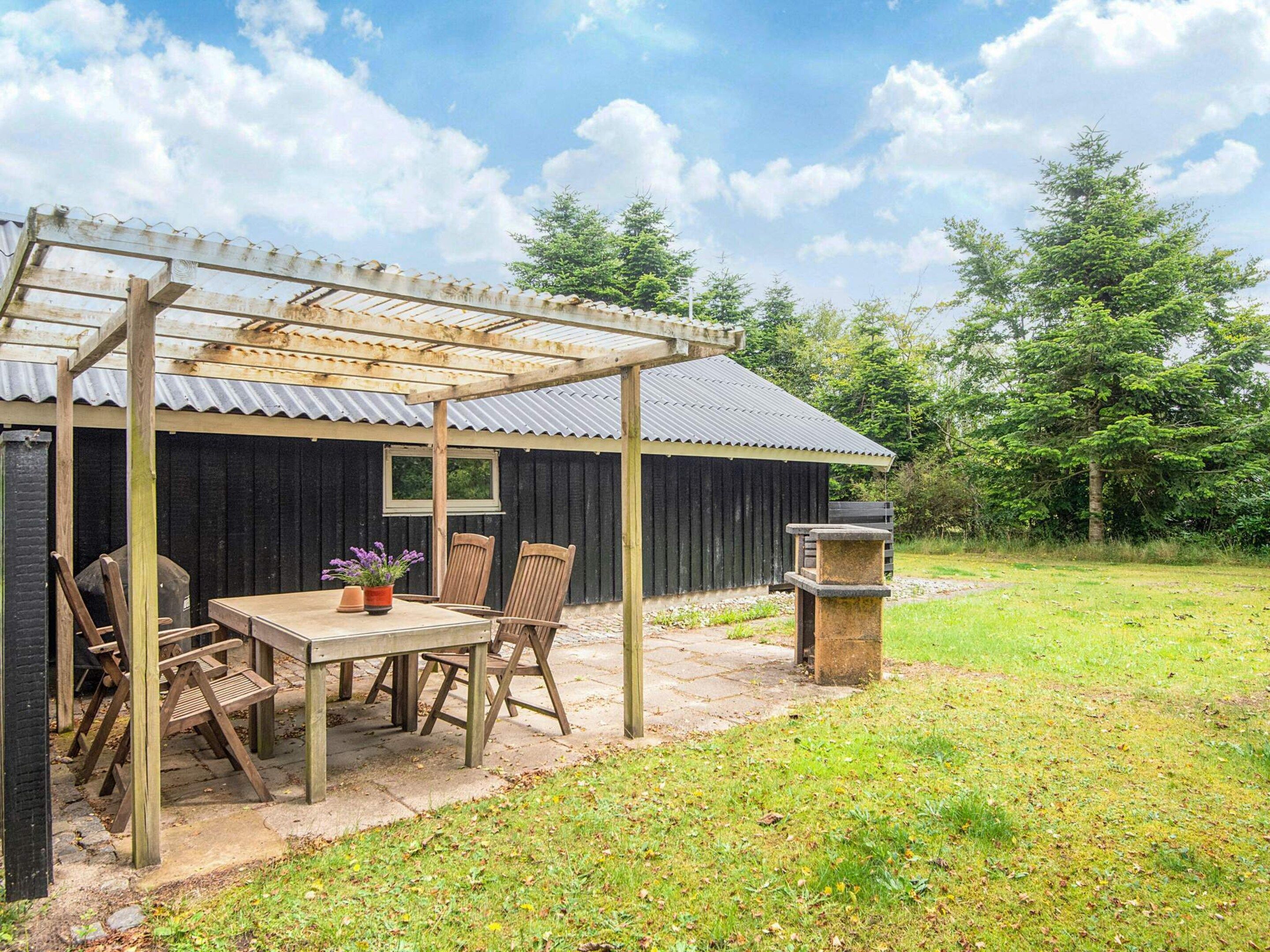 A rustic outdoor seating area with a wooden table and chairs, a pergola, and a stone planter.