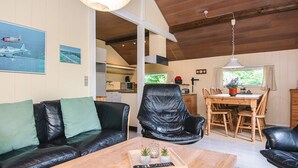 A cozy living room with a black leather sofa, a wooden coffee table with a remote control, and a dining area with a wooden table and chairs. - 4 Person Holiday Home in Skjern (Skjern)