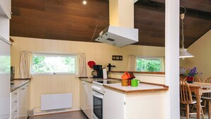 A compact kitchen with wooden cabinets, a built-in oven, a coffee maker, and a dining area with a wooden table and chairs. - 4 Person Holiday Home in Skjern (Skjern)