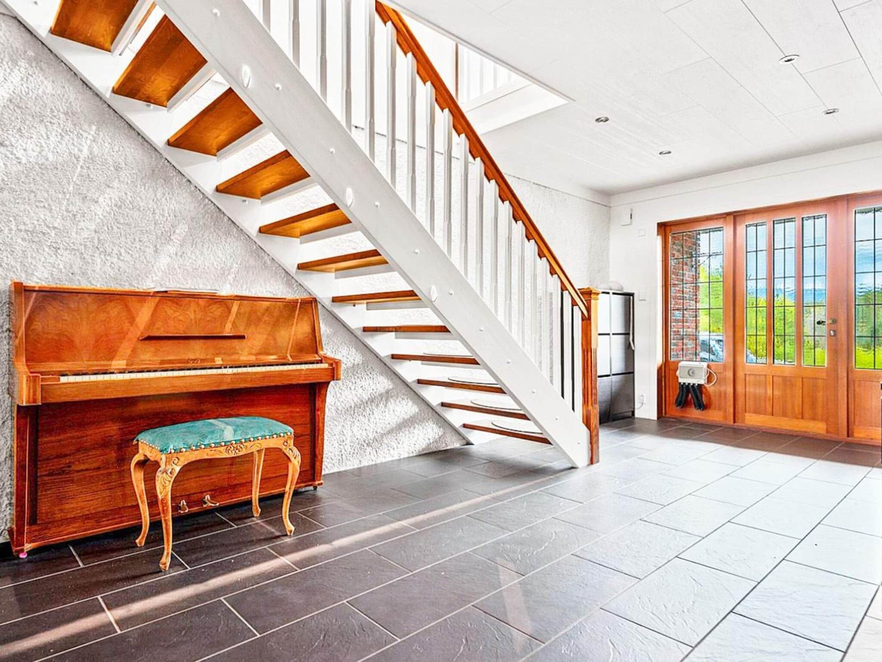 A grand piano, a staircase, and a view of the outdoors.