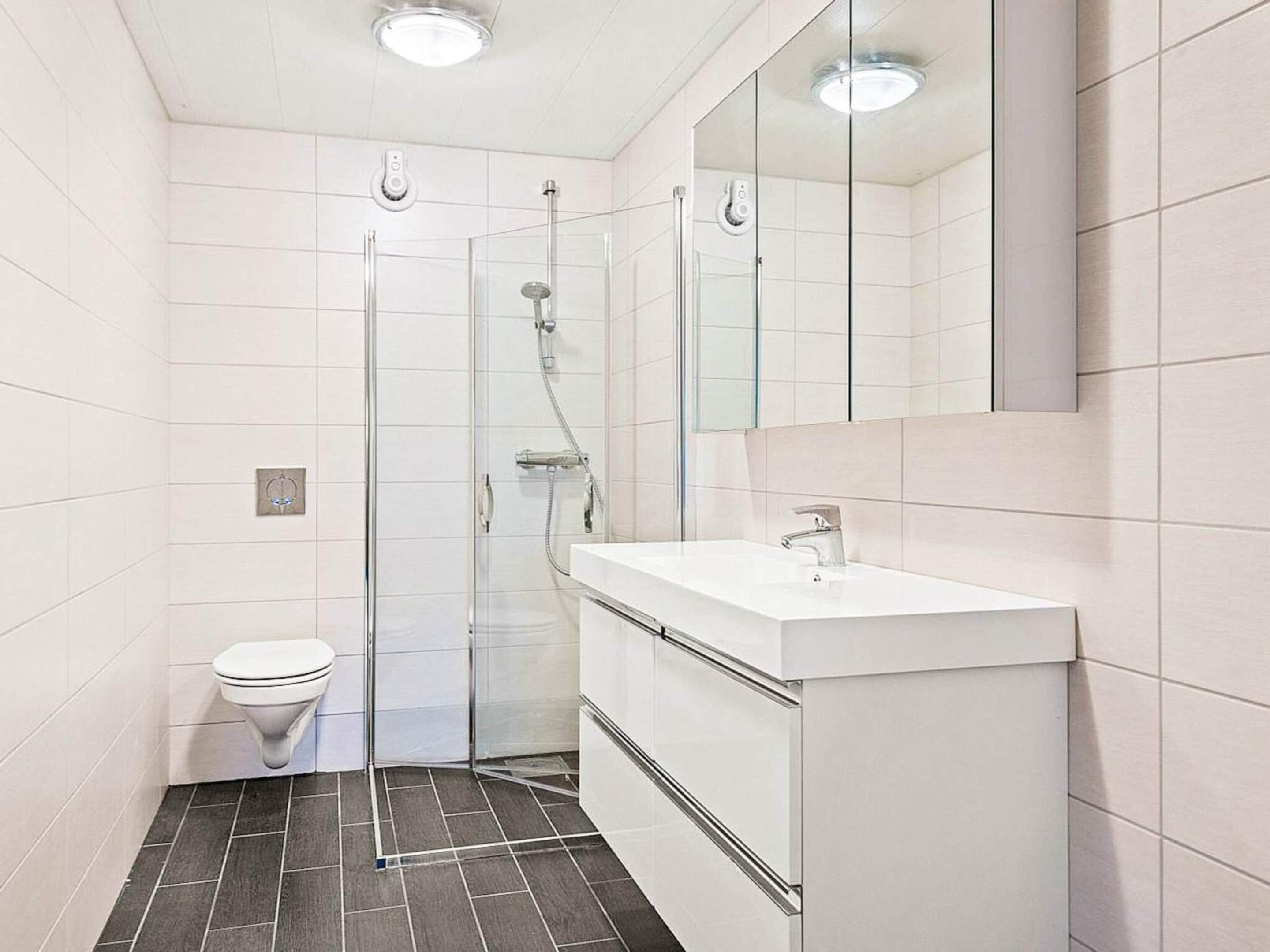 A modern bathroom with a glass shower enclosure, a white sink, and a toilet.