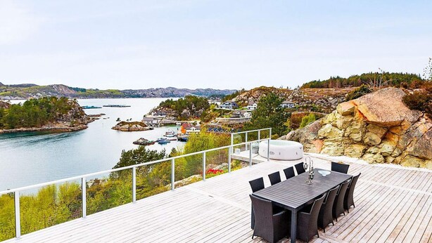 A wooden deck with a table and chairs overlooking a body of water with boats and houses in the background.