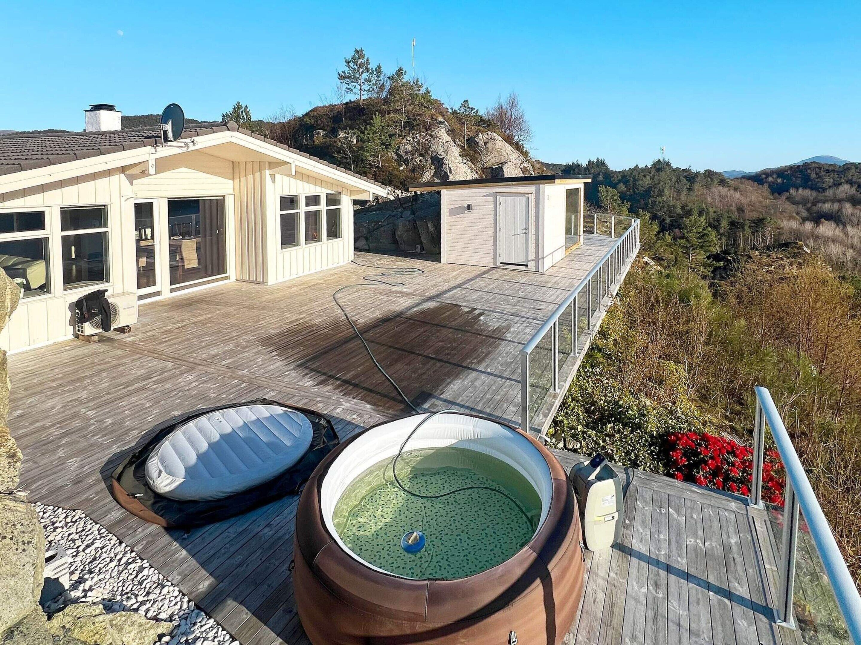 A rooftop with two hot tubs, a wooden deck, and a view of a mountainous landscape.