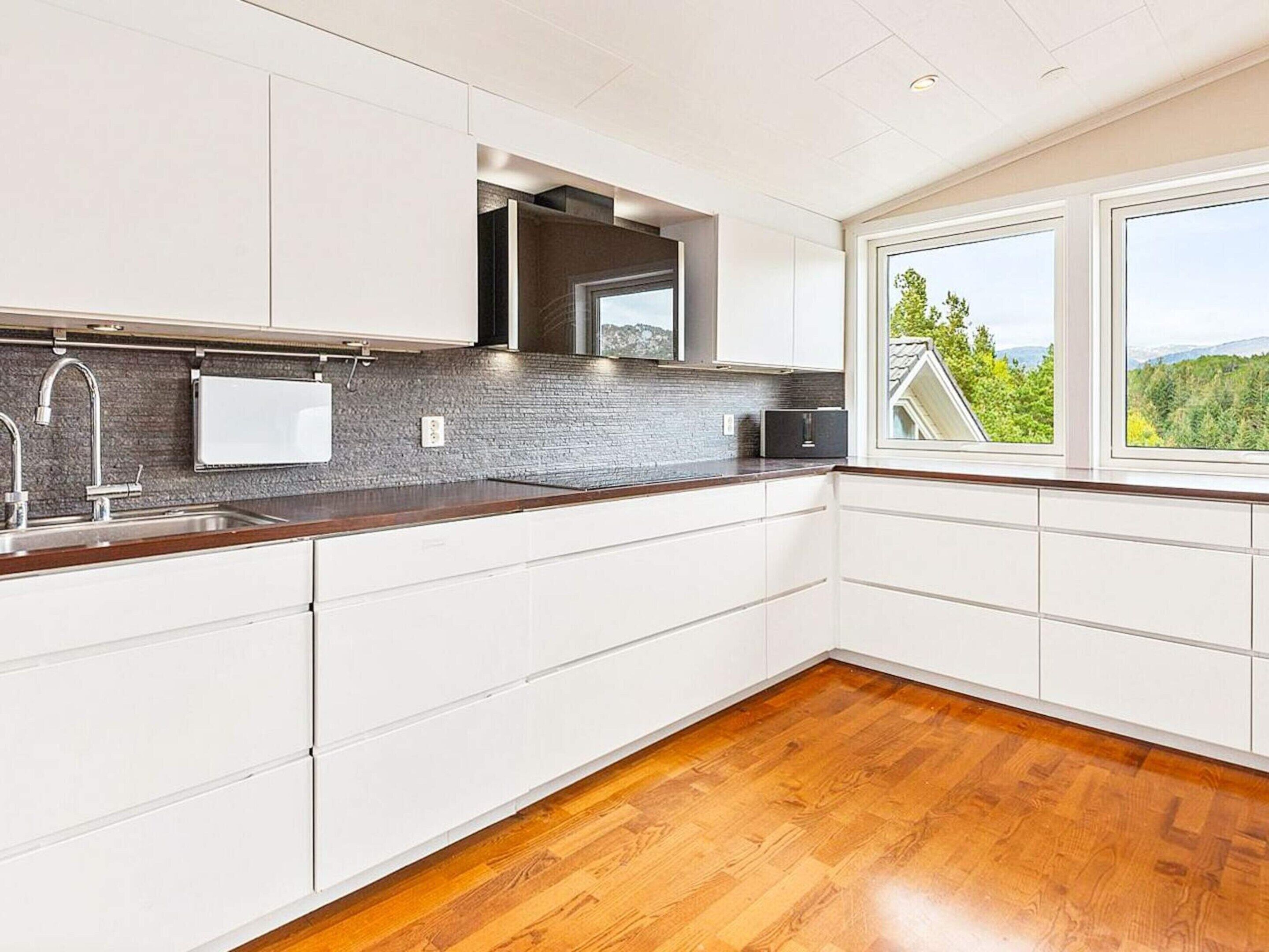 A modern kitchen with white cabinetry, a stainless steel sink, and a view of greenery outside.
