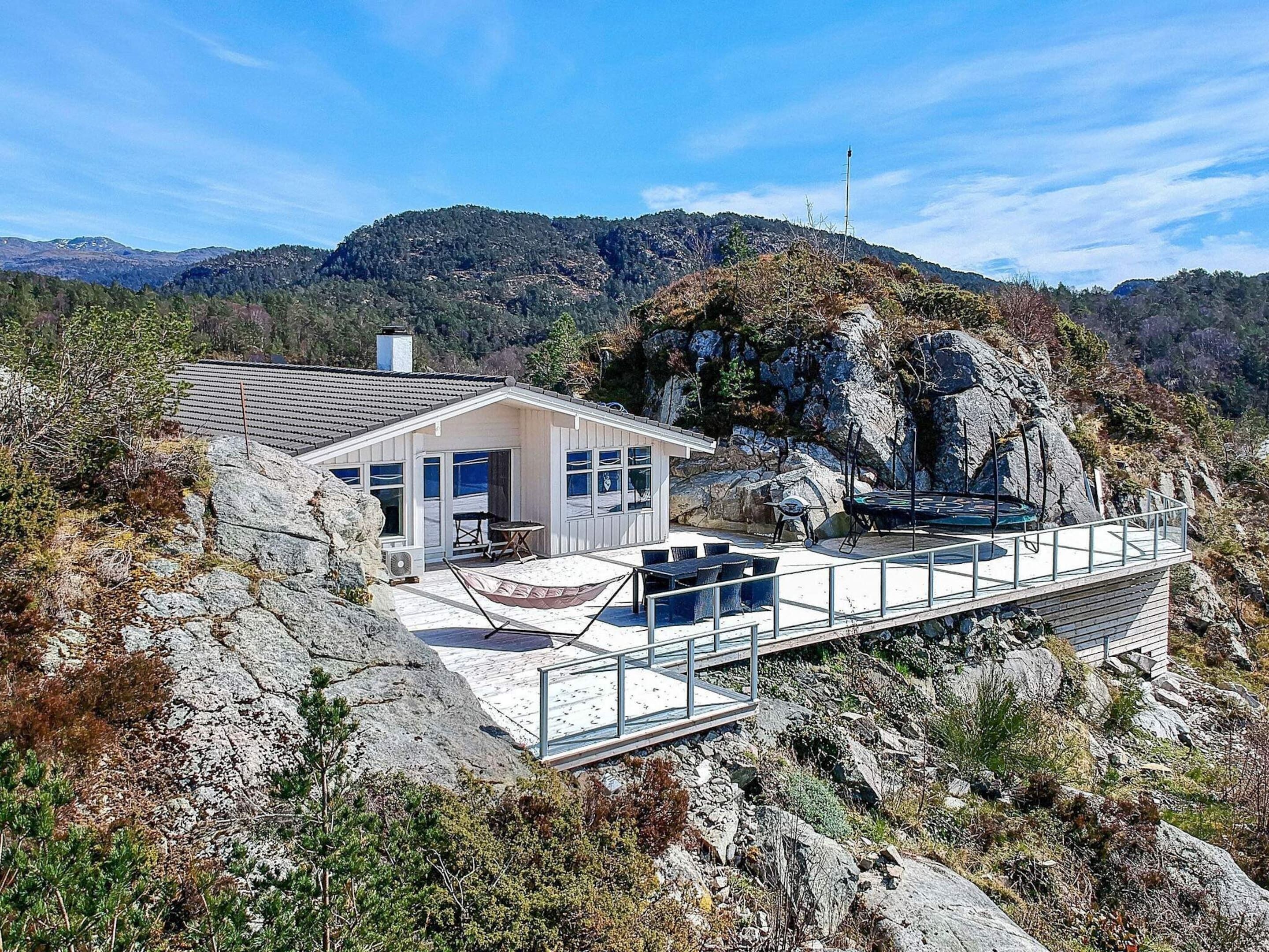 Una cabaña con un porche, un trampolín y vistas de las montañas circundantes.