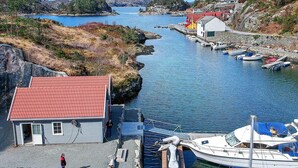 A coastal marina with boats docked, a small building with a red roof, and a rocky shoreline.